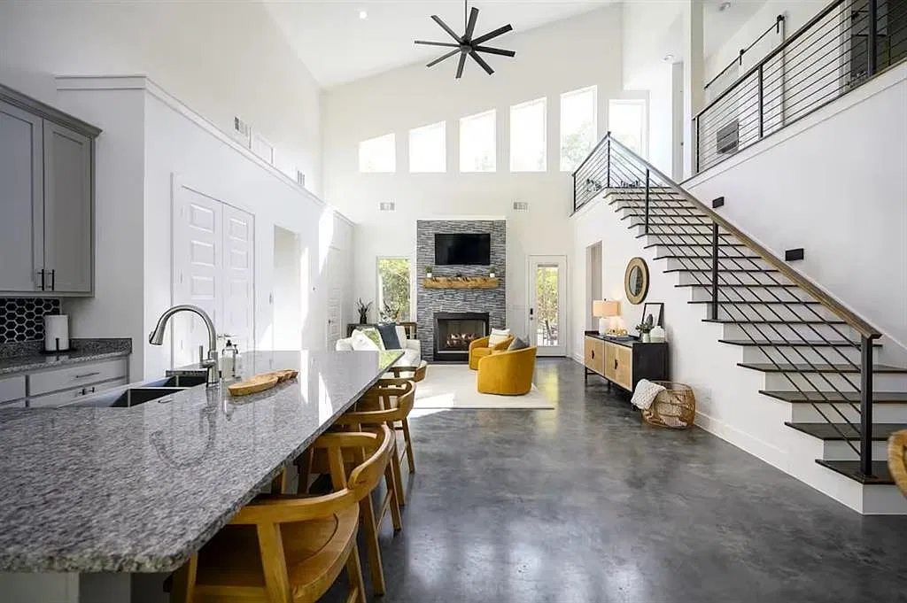 Kitchen island and great room under a high ceiling with a steel-railed staircase